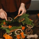 Alameda Post - a person makes a wreath out of natural materials including evergreen, pinecones, and dried oranges