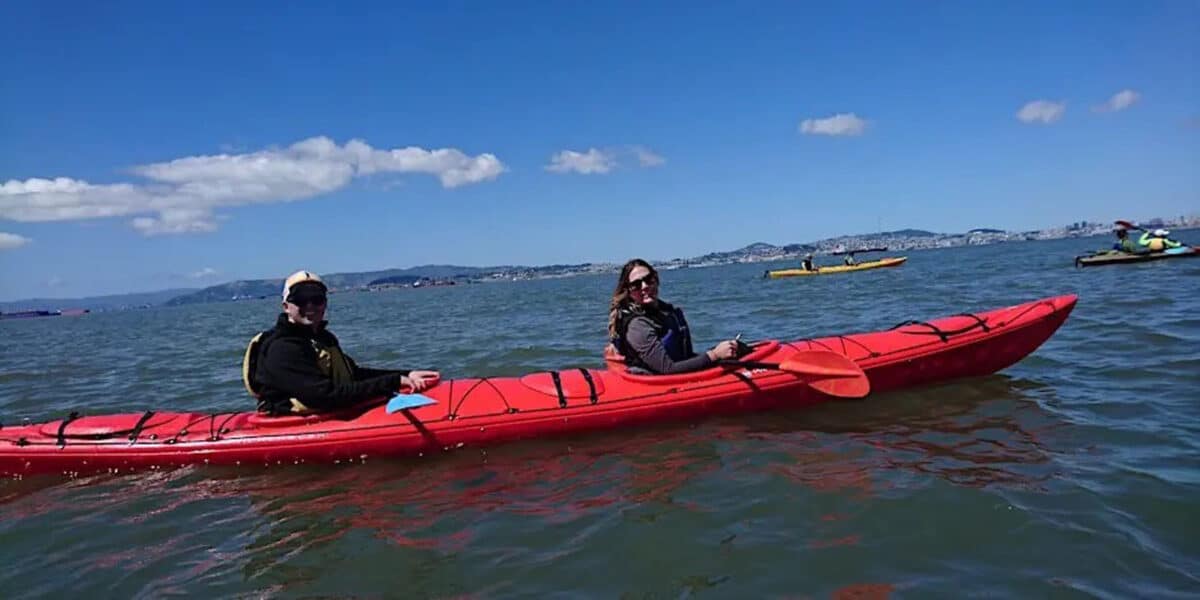 Alameda Post - Two kayakers smile at the camera from their double kayak. 