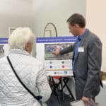 Alameda Post - a staff member points at a map of the Oakland Alameda Access Project plans and speaks to a white haired, older community member