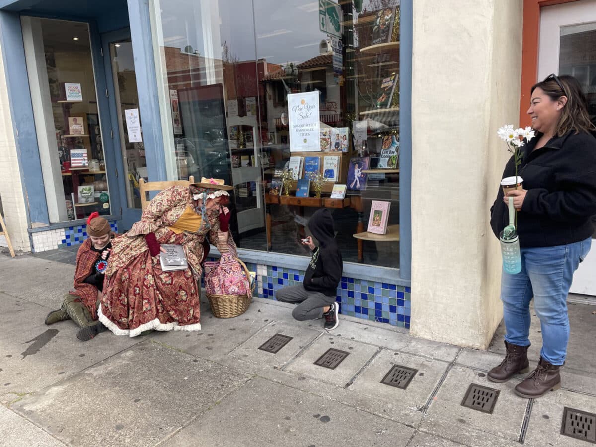 Alameda Post - A woman in a Mother Goose costume sits outside of Books Inc and chats with a child. 