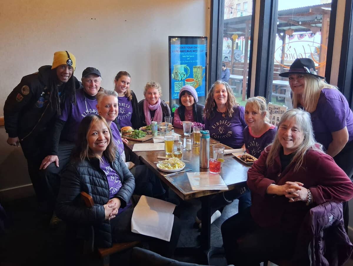 Alameda Post - Eleven smiling people in purple Kindness Coalition shirts sit at a table. 