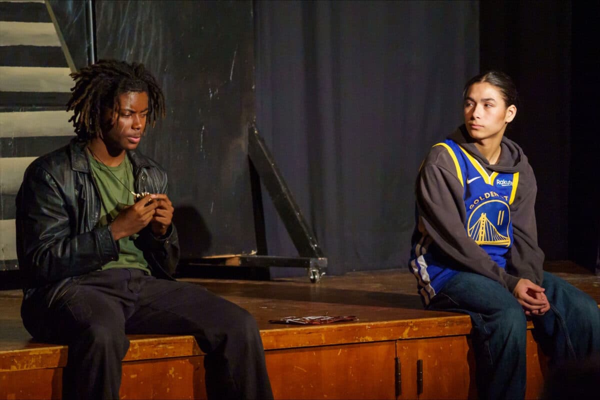 Alameda Post - Two actors sit on the end of the stage and talk to one another.