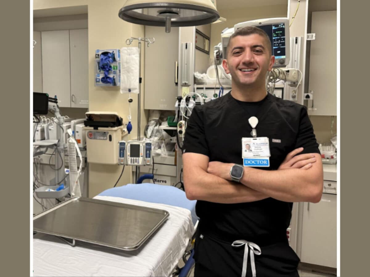 Alameda Post - An emergency room doctor stands in an operating room and smiles at the camera.