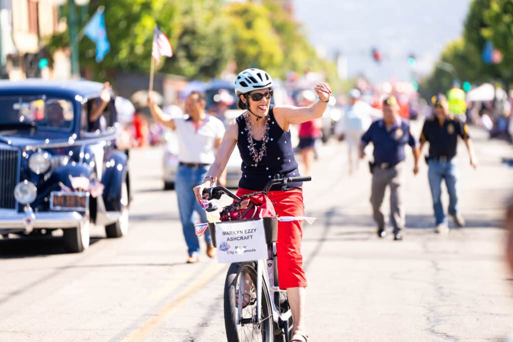 Alameda Post - Alameda Mayor Ashcraft rides a bicycle in the 4th of July Parade
