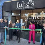 Alameda Post - six people stand outside of Julie's Coffee and Tea Garden as the new owner cuts a large ribbon