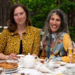 Alameda Post - Shannon Marsden and Julie sit and smile at the camera. They are seated at a table decorated with a fancy spread of tea and food
