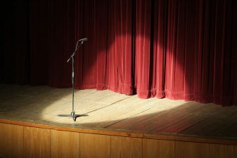 Alameda Post - A microphone onstage with a spotlight in front of a red velvet curtain.
