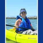Alameda Post - a woman smiles broadly while sitting in a kayak on the water