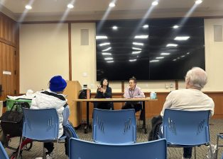 Alameda Post - The Home Match director and another person sit at the front of a room at the library and talk.