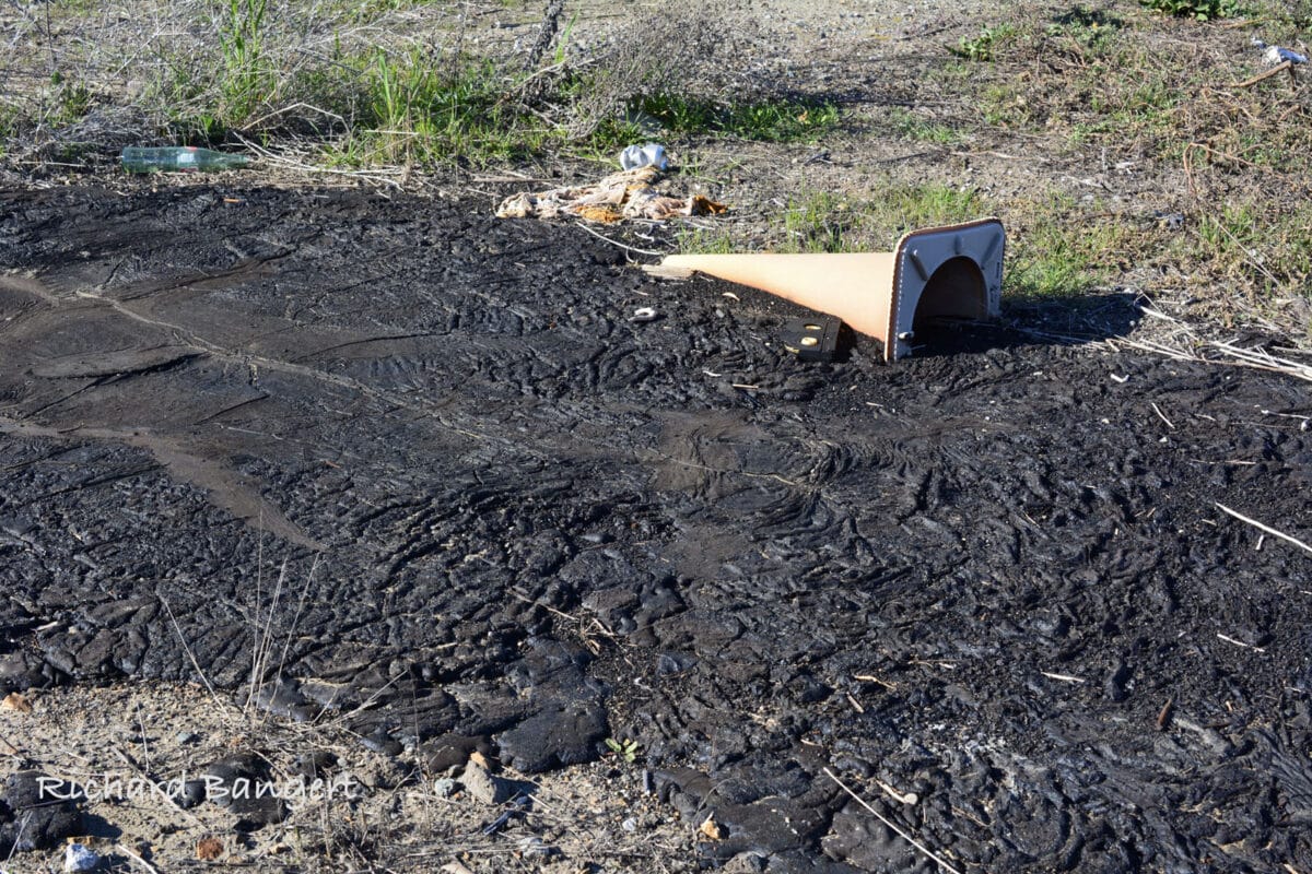 Alameda Post - A large patch of dried tar in a field, with a traffic cone stuck in it.