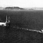 Alameda Post - a tug boat moves Utah Construction's dredge through the water of the San Fransisco Bay. Old black and white photo.