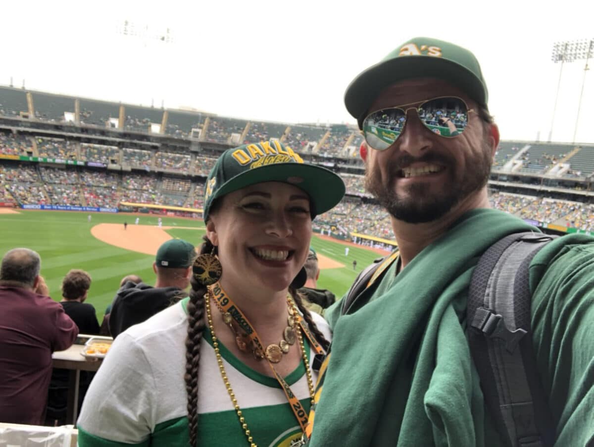 Alameda Post - a man and woman take a selfie in the stands of an Oakland A's game