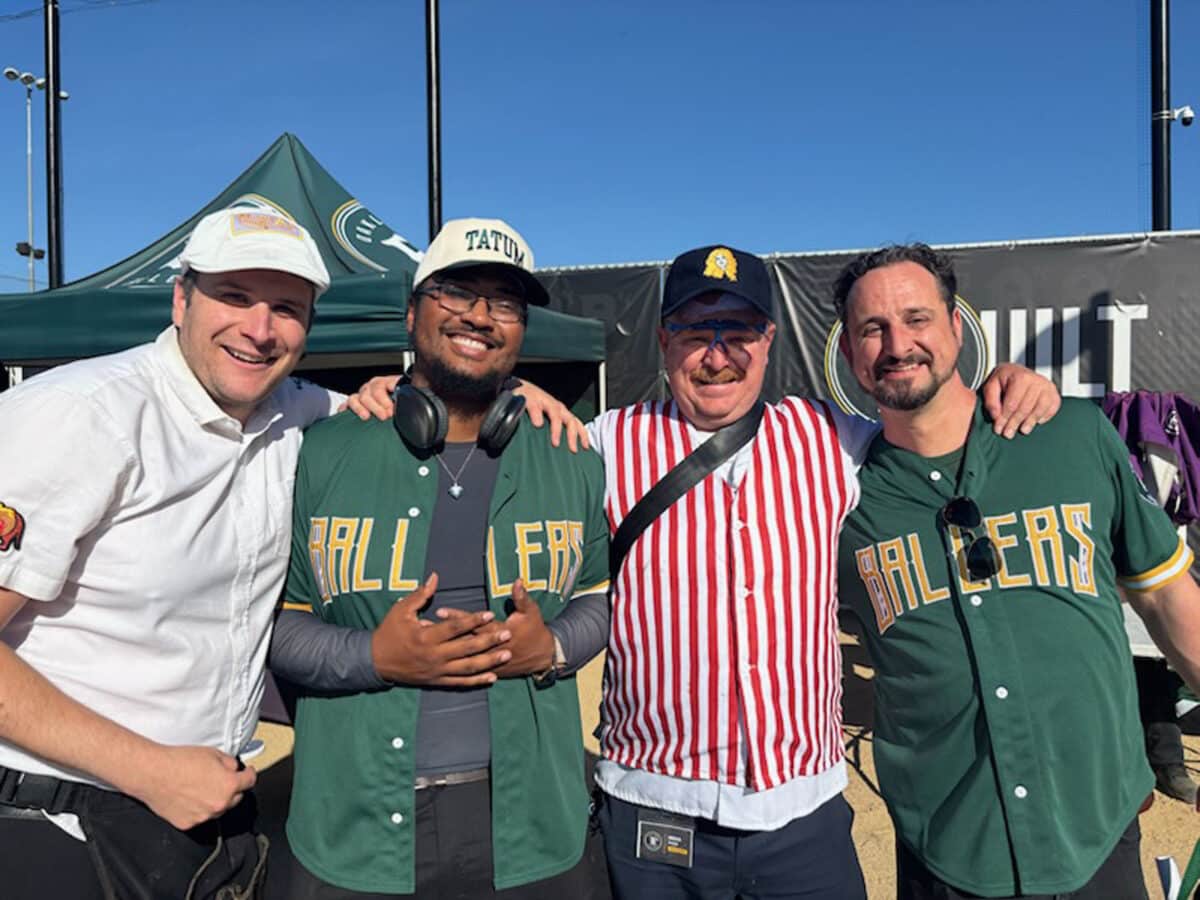 Alameda Post - four men smile at the camera. They are all dressed to attend a baseball game.